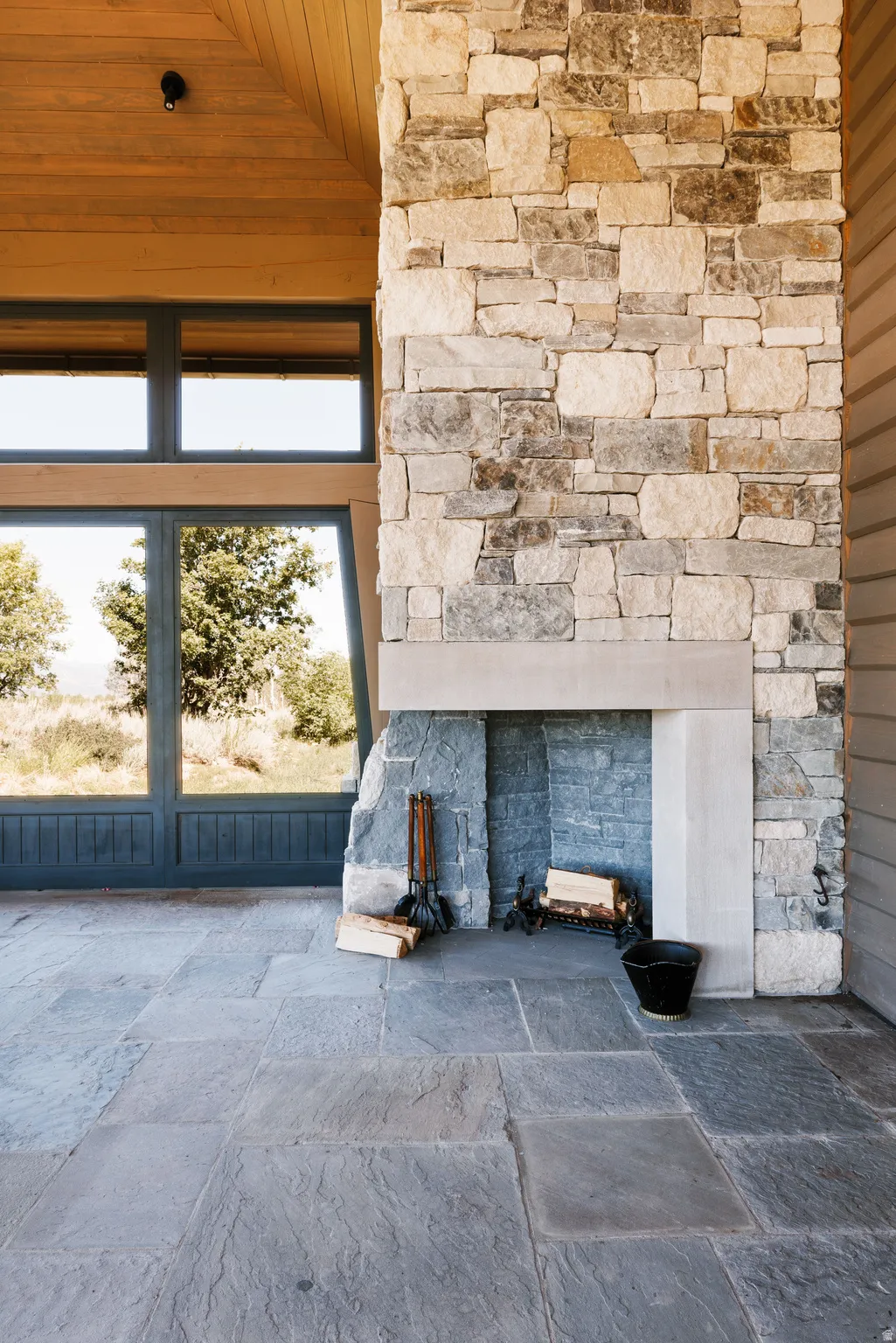 Exterior stone fireplace with a stone hearth, featuring a natural stone facade and custom dark-framed windows