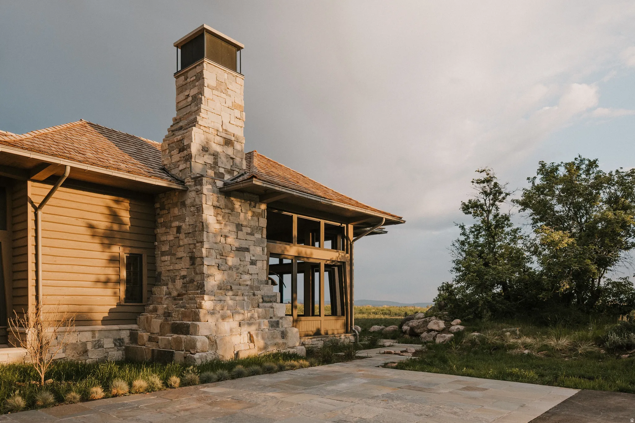 Stone chimney with a metal cap, horizontal siding, and a gabled roofline