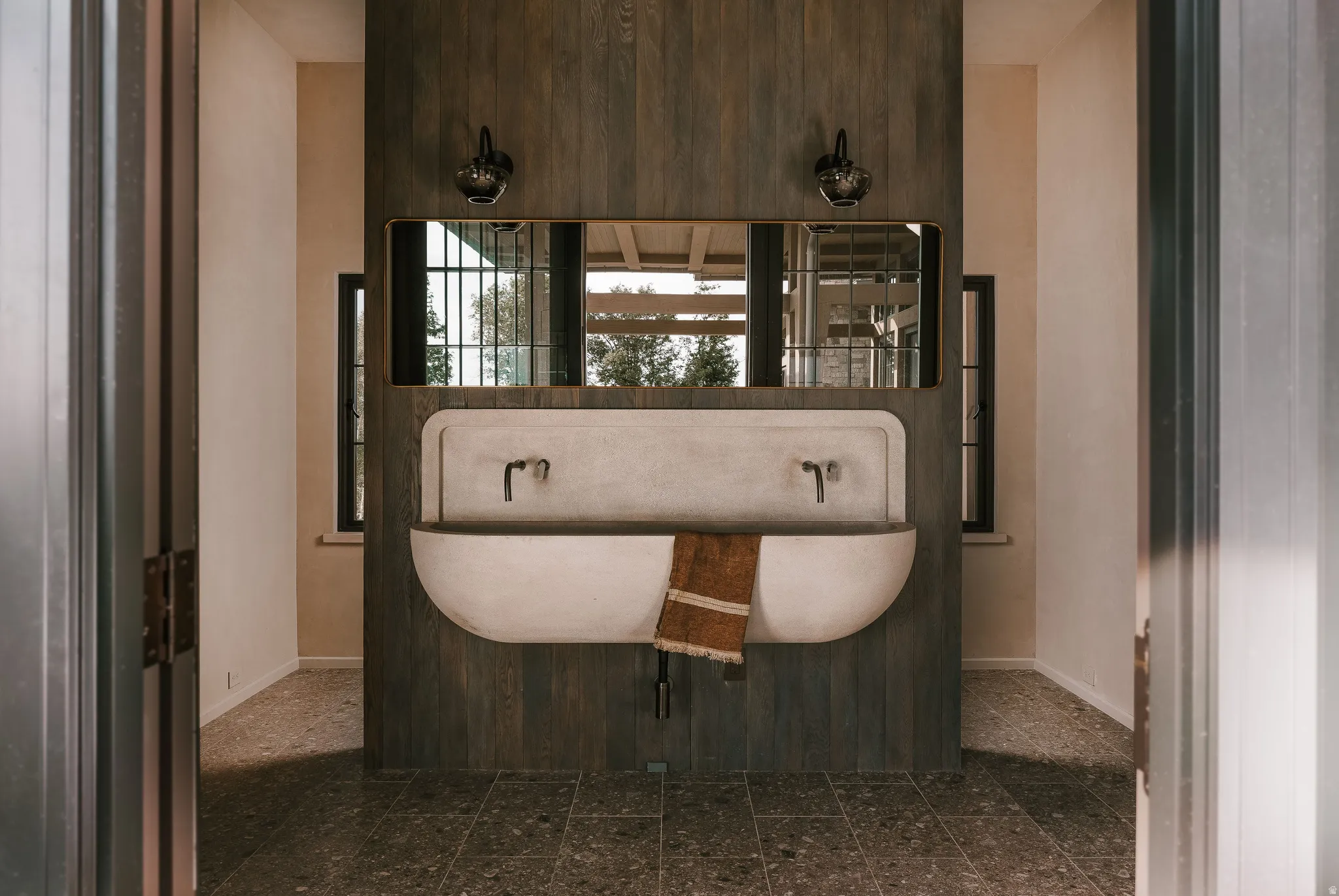 Integrated concrete trough sink with two wall-mounted faucets, set against a dark wood-paneled wall