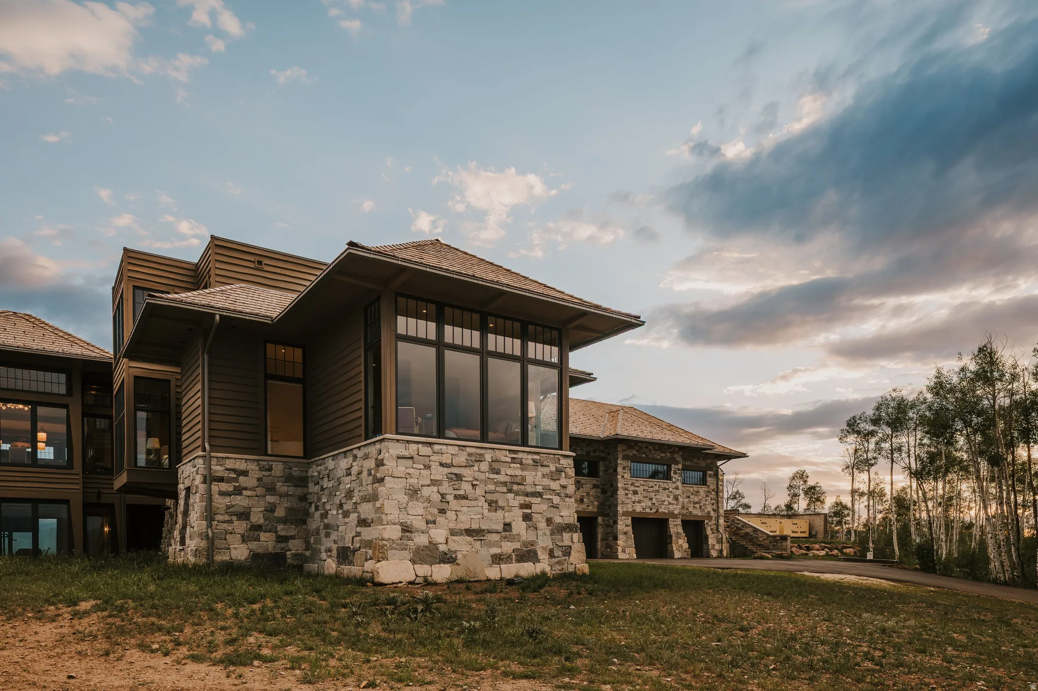 Multi-level property featuring extensive stone veneer, horizontal wood siding, and multiple large windows with dark frames