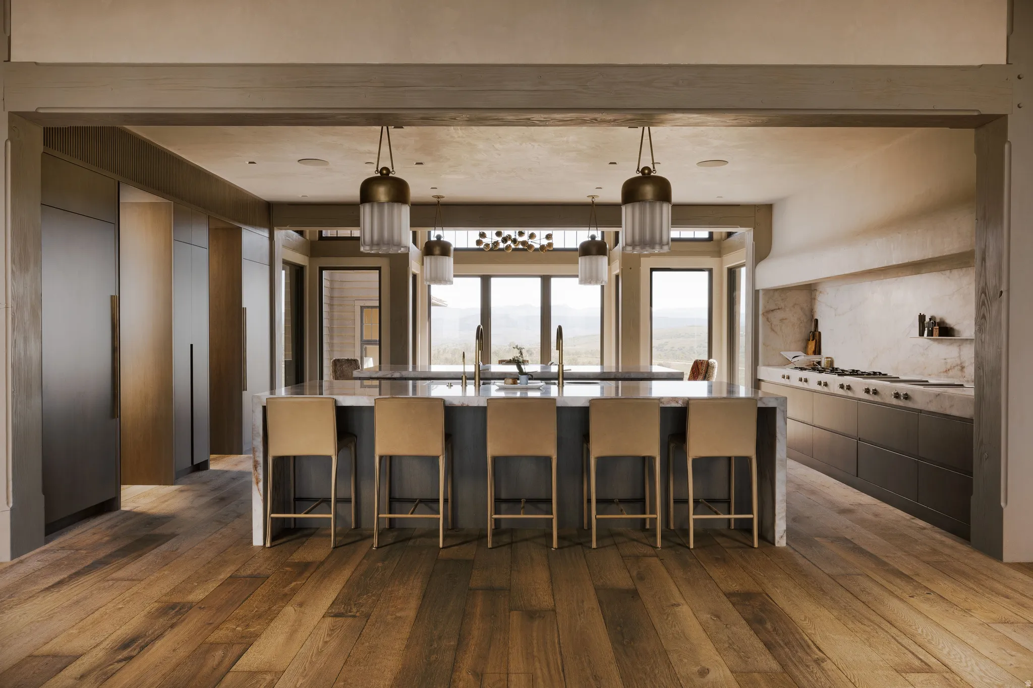 Spacious kitchen featuring a large island with seating, a professional-grade range, integrated refrigeration, warm wood-finish flooring, and multiple pendant light fixtures