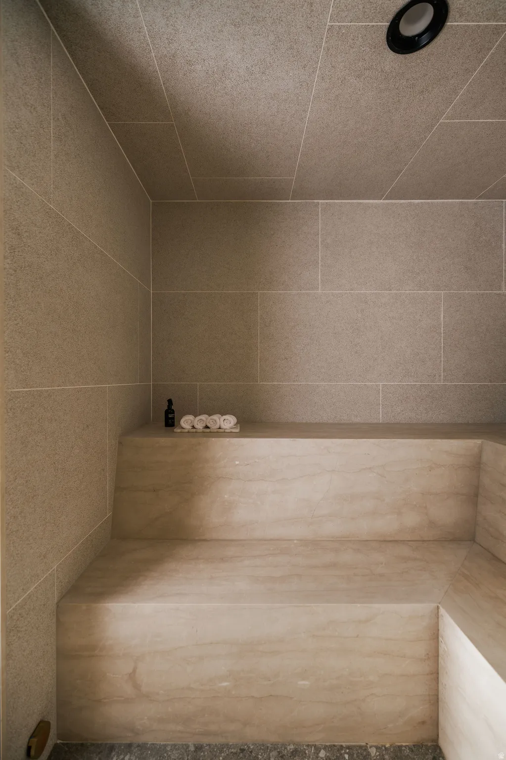 Built-in stone bench with subtle veining, complemented by large format wall and ceiling tiles