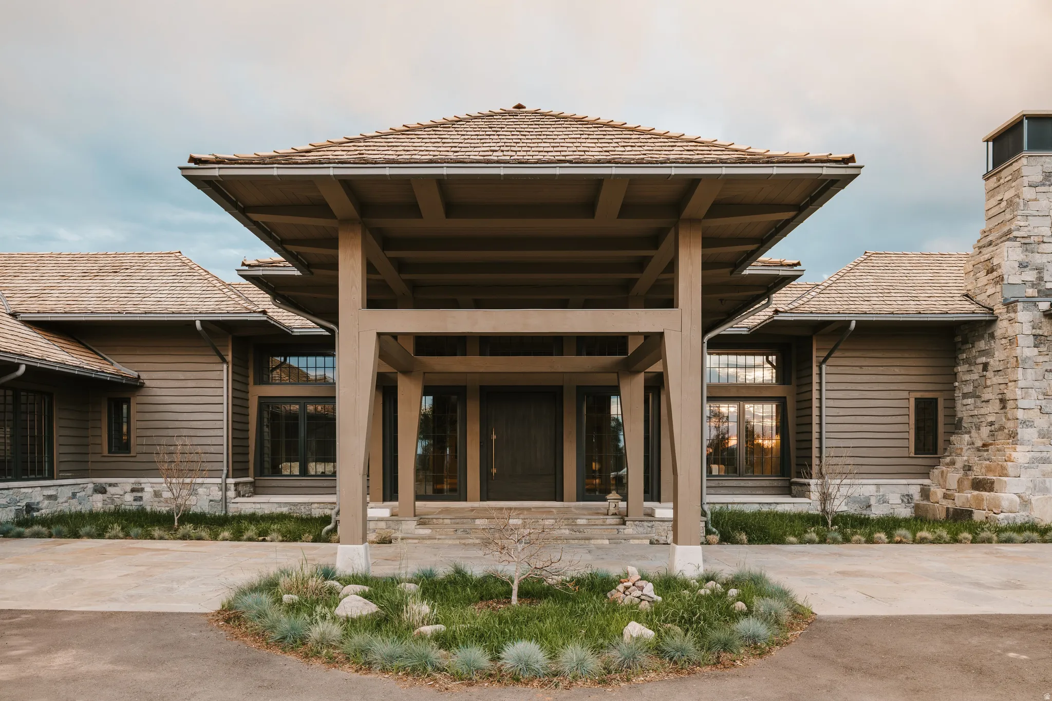 Architectural residence featuring a prominent covered entry, wood shingle roofing, horizontal siding, stone veneer foundation, and a stone chimney