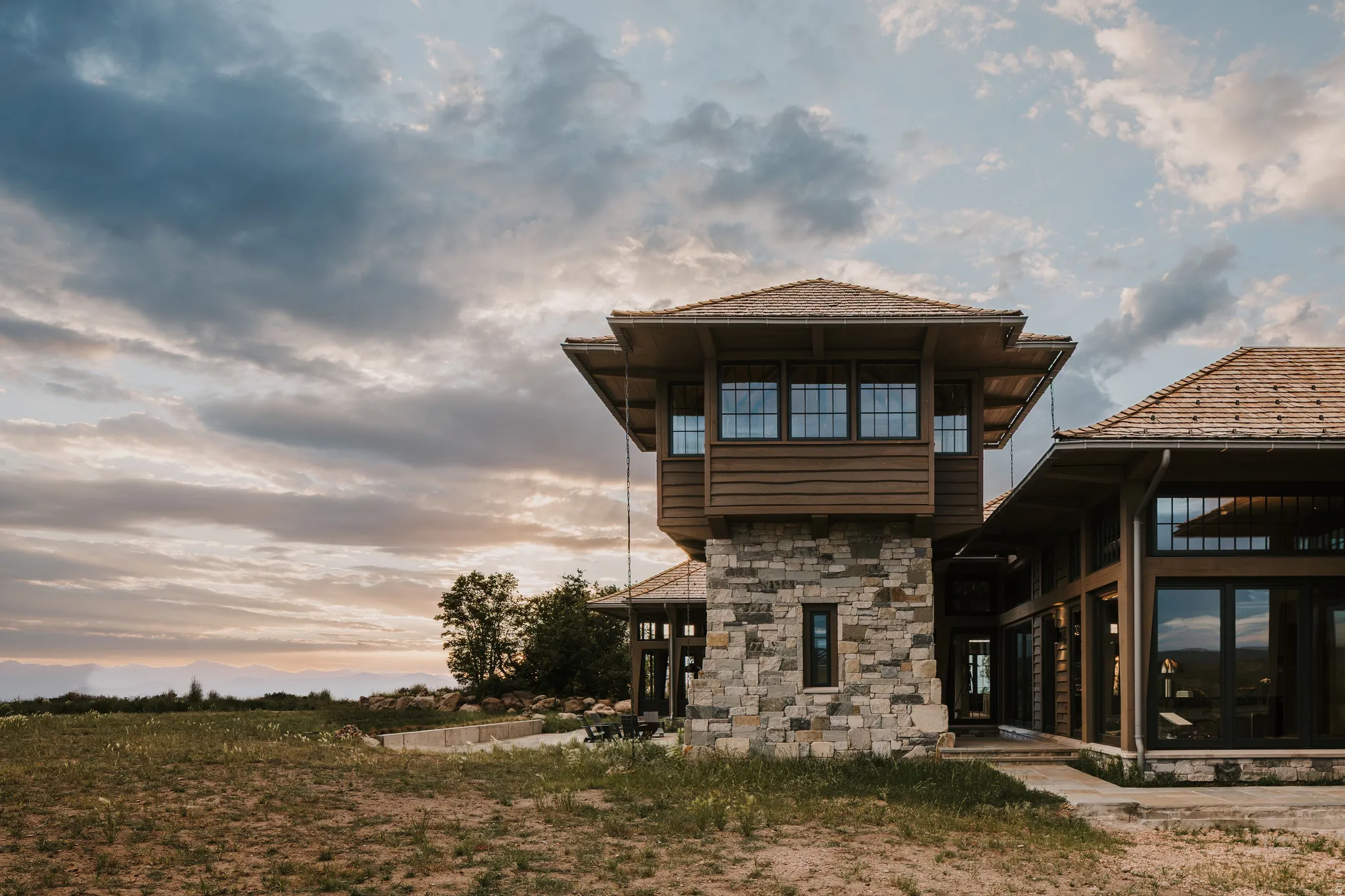 Craftsman-style architecture featuring a prominent stone tower with a wood-sided upper level, multiple windows, and a shingle roof