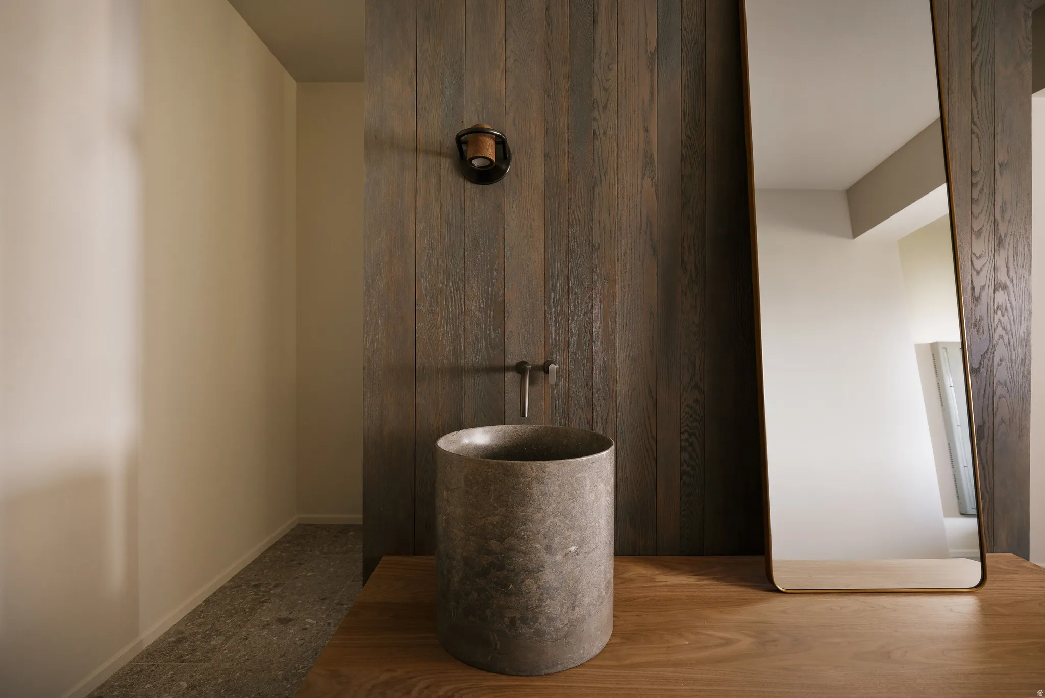 Vanity area featuring a cylindrical stone basin, wall-mounted faucet, and wood-finish countertop