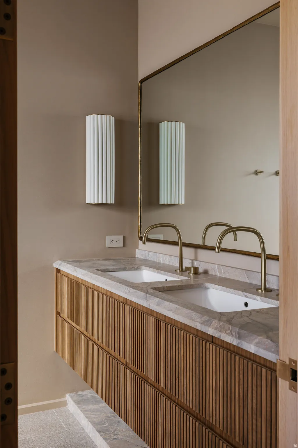 Floating wood-slat vanity featuring dual undermount sinks with brass fixtures and a stone countertop
