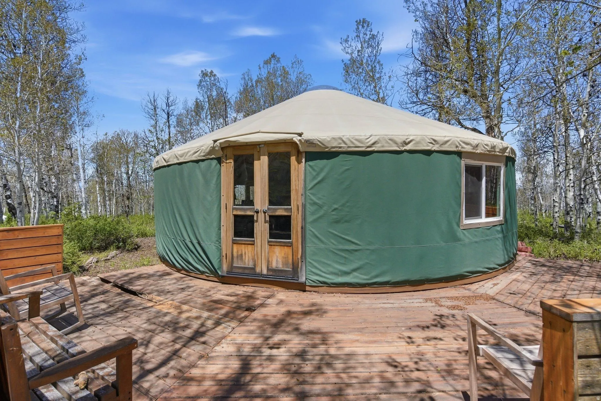 Green yurt with a light-colored roof and natural wood double doors