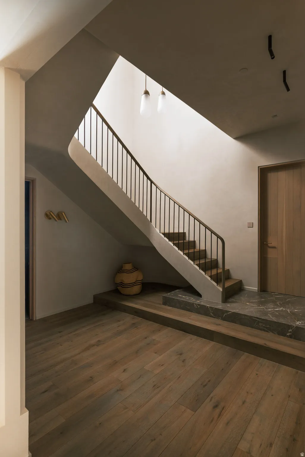 Curved staircase with dark metal railing, wood-finish flooring, and a marble-finish landing