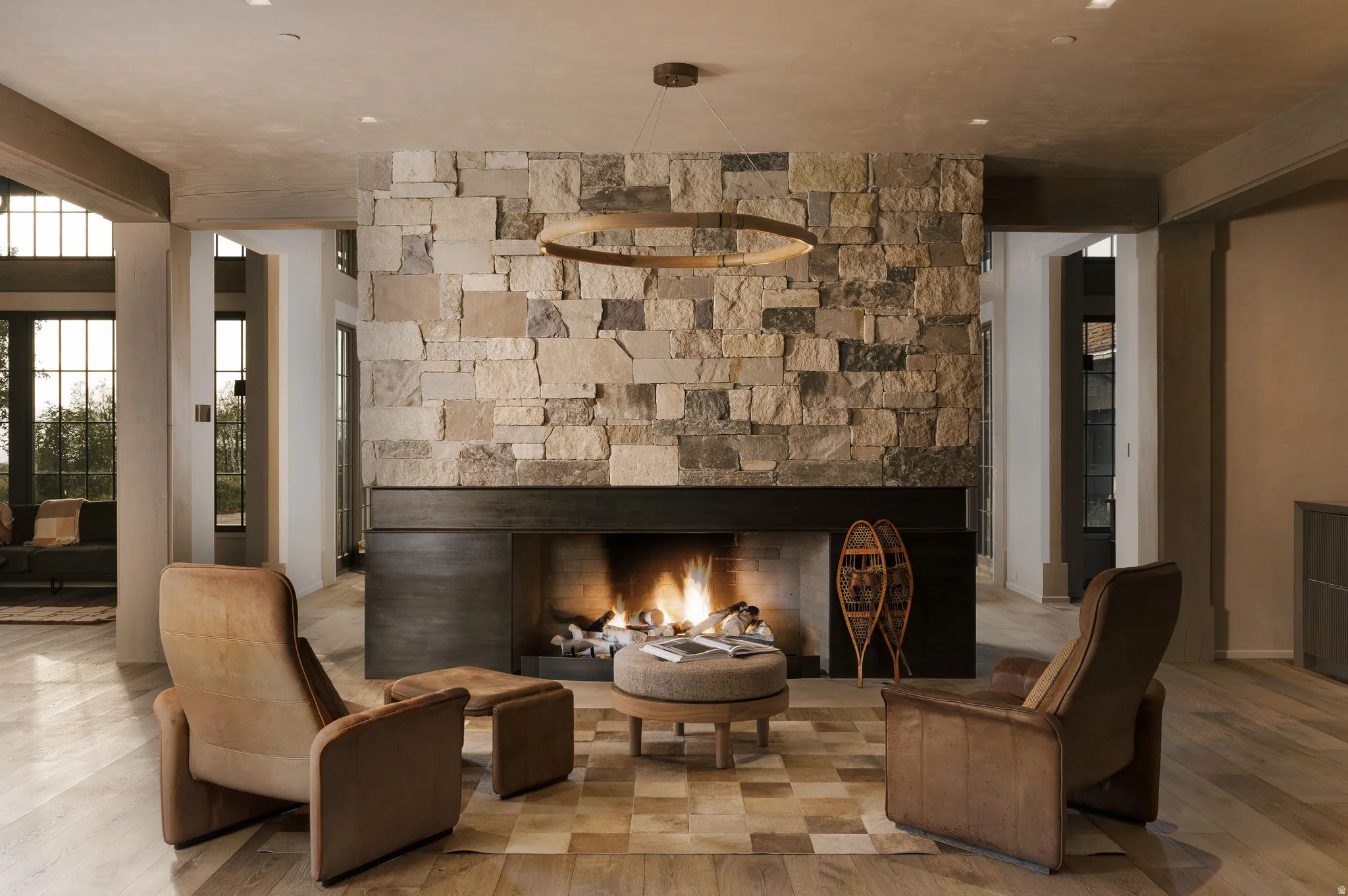 Central stone fireplace featuring a dark metal mantel, wood-finish flooring, and recessed ceiling lighting
