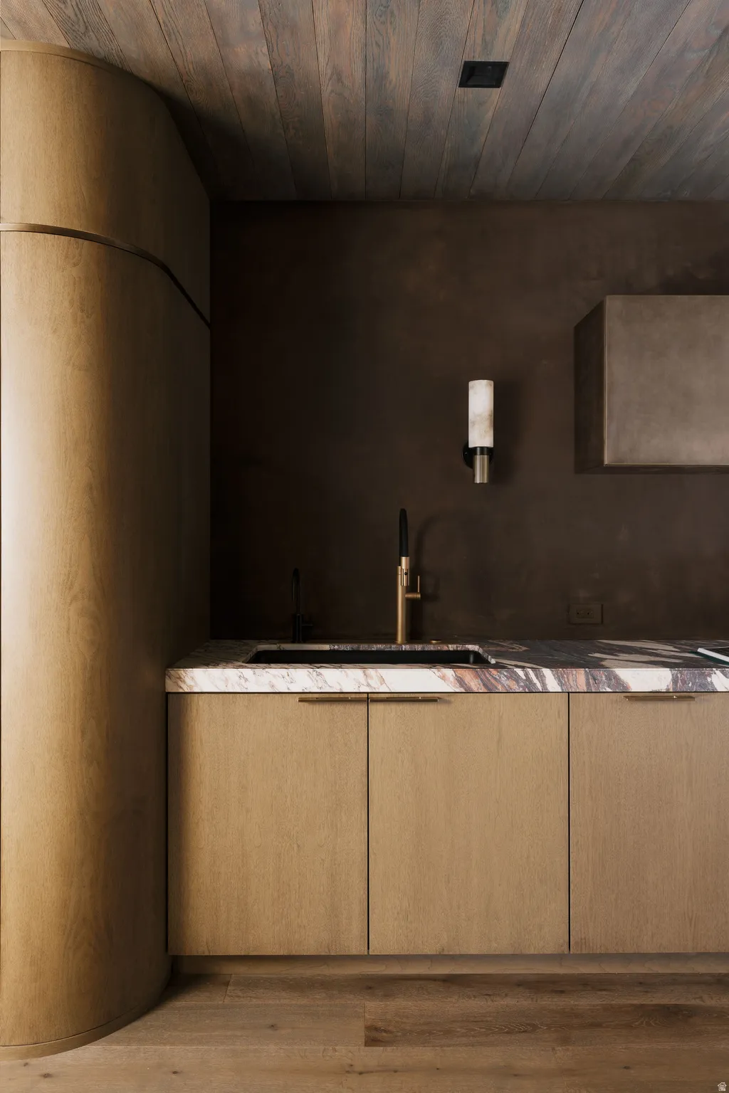 Custom wood-finish cabinetry featuring integrated hardware, a contrasting stone countertop with an under-mount sink, and a modern wall-mounted faucet