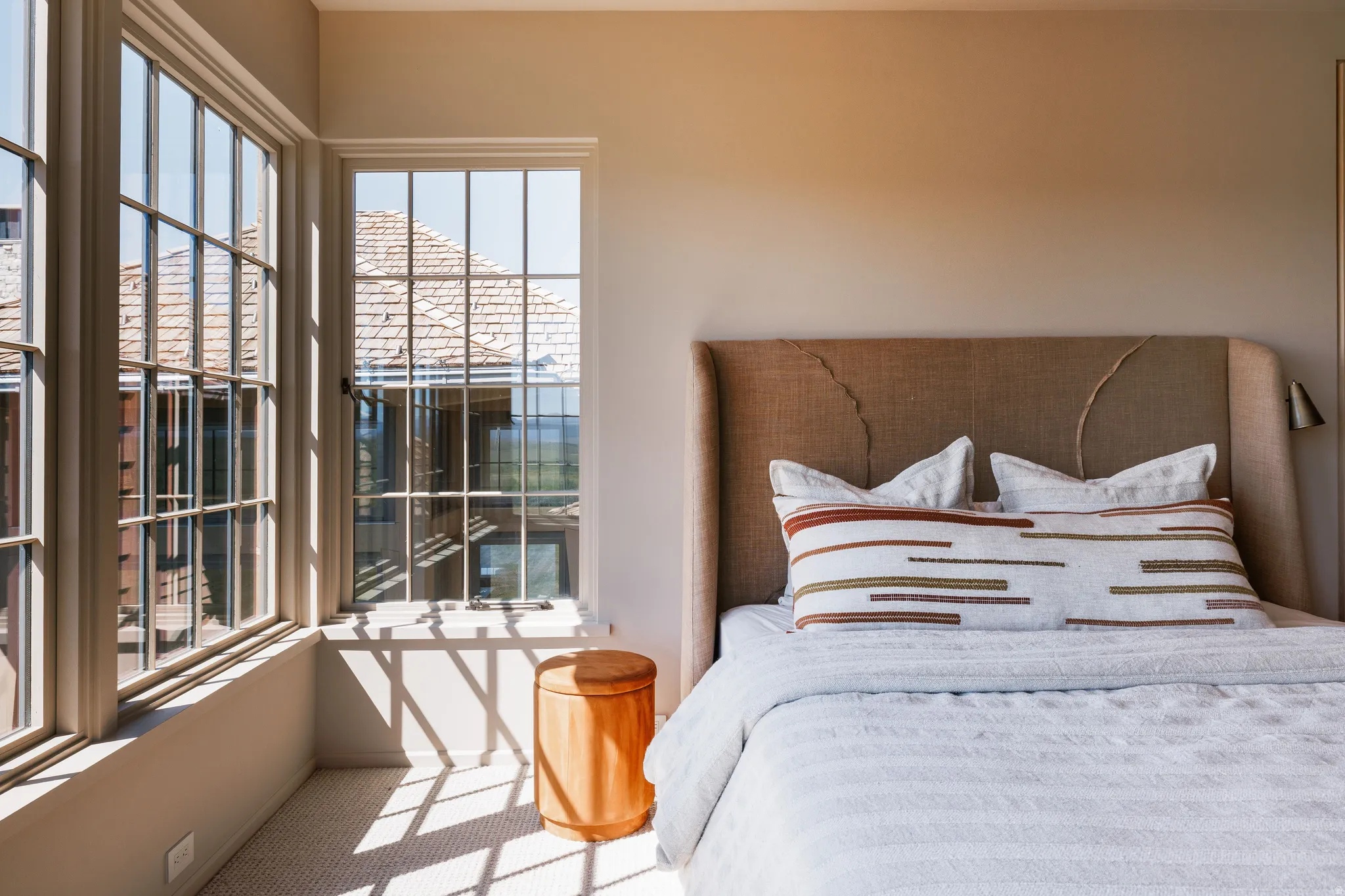 Bedroom featuring multiple grid-pattern windows, light-toned carpeting, and a textured upholstered headboard with integrated sconces