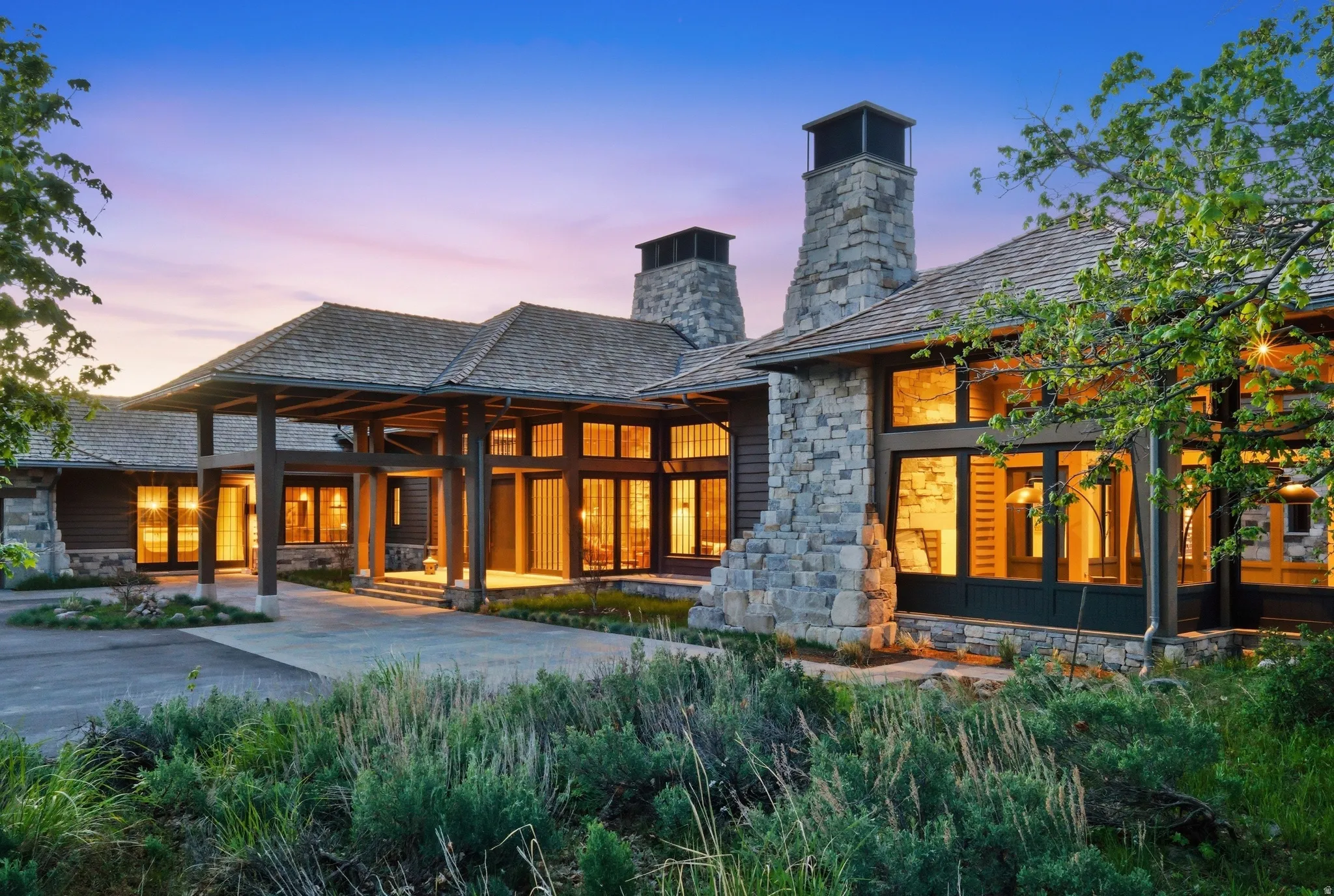 Stone and timber exterior featuring multiple large picture windows, a covered porte-cochère entrance, and two prominent stone chimneys