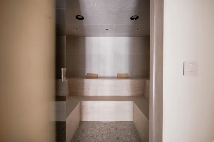 Steam room featuring tiled walls, built-in benches, recessed lighting, and a pebble-finish floor