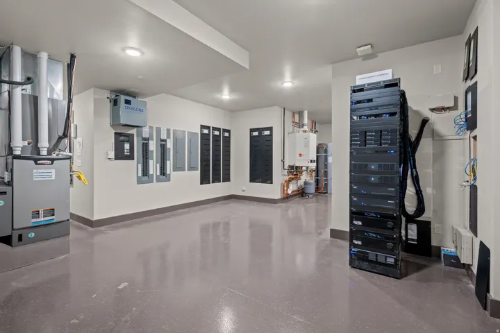 Dedicated utility room featuring a furnace, multiple electrical panels, an extensive server rack, and water heaters