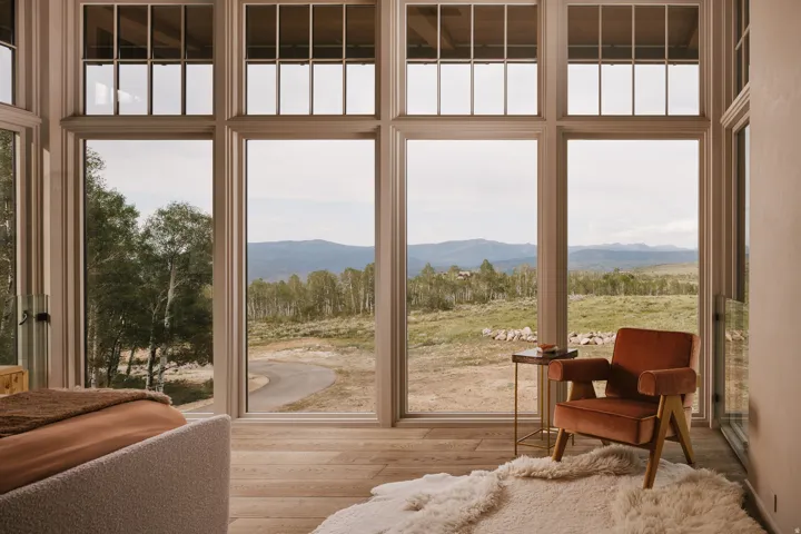 Floor-to-ceiling windows with upper transoms frame mountain and tree scenery