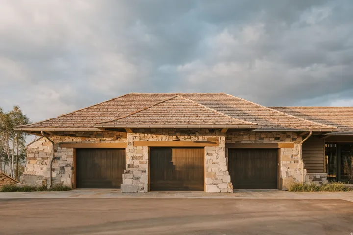 Stone and wood-sided exterior featuring three garage bays with wood plank doors