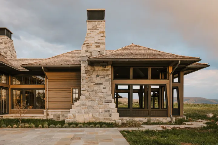 Contemporary architecture featuring a wood shake roof, stone chimneys, and expansive window walls