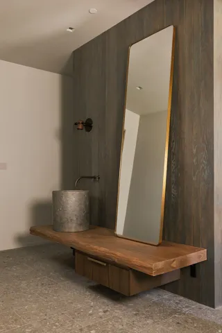 Floating wood-finish vanity with an integrated drawer, complemented by a stone vessel sink and wall-mounted faucet