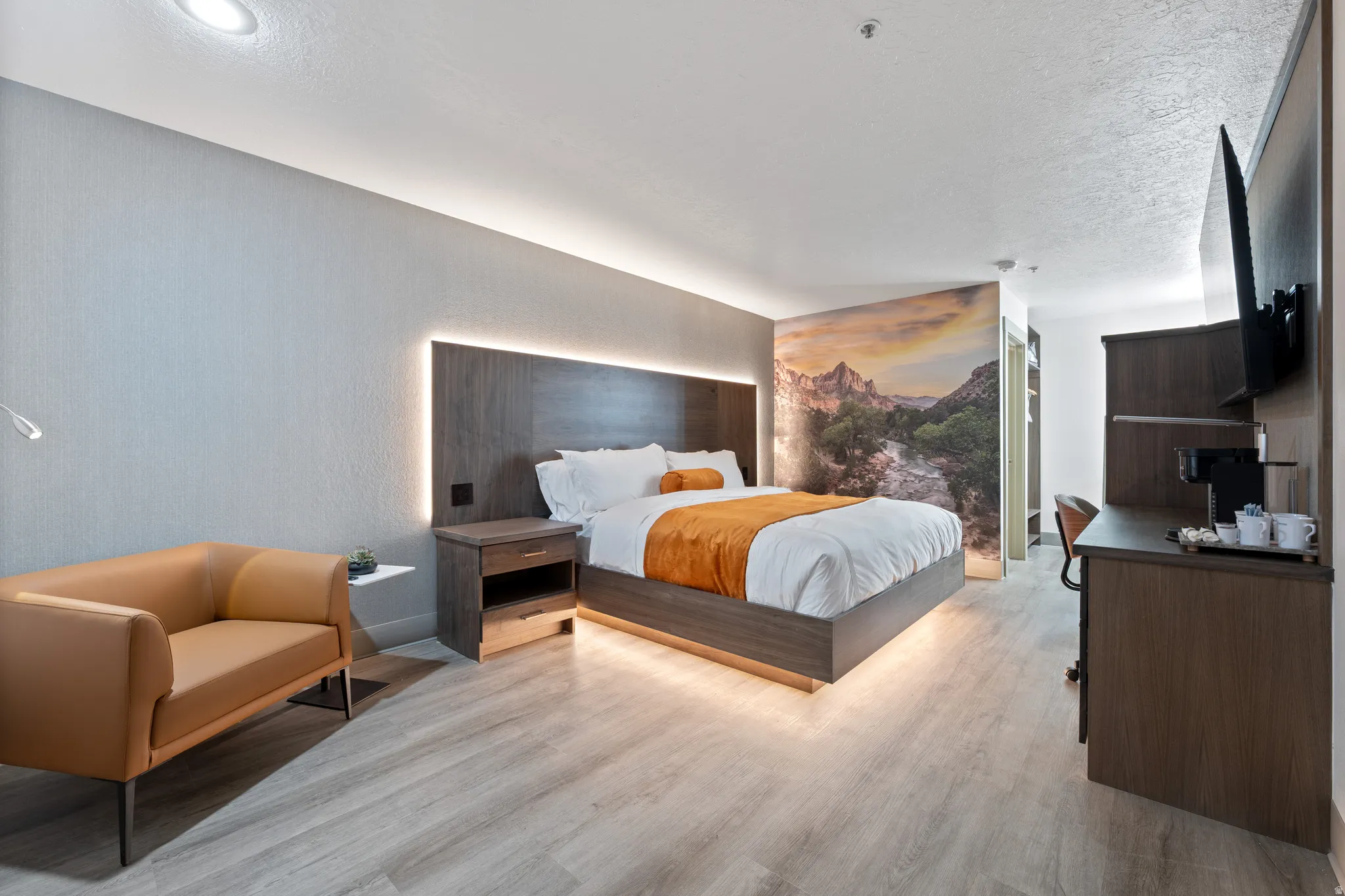 Contemporary bedroom featuring wood-finish flooring and a built-in headboard with integrated lighting