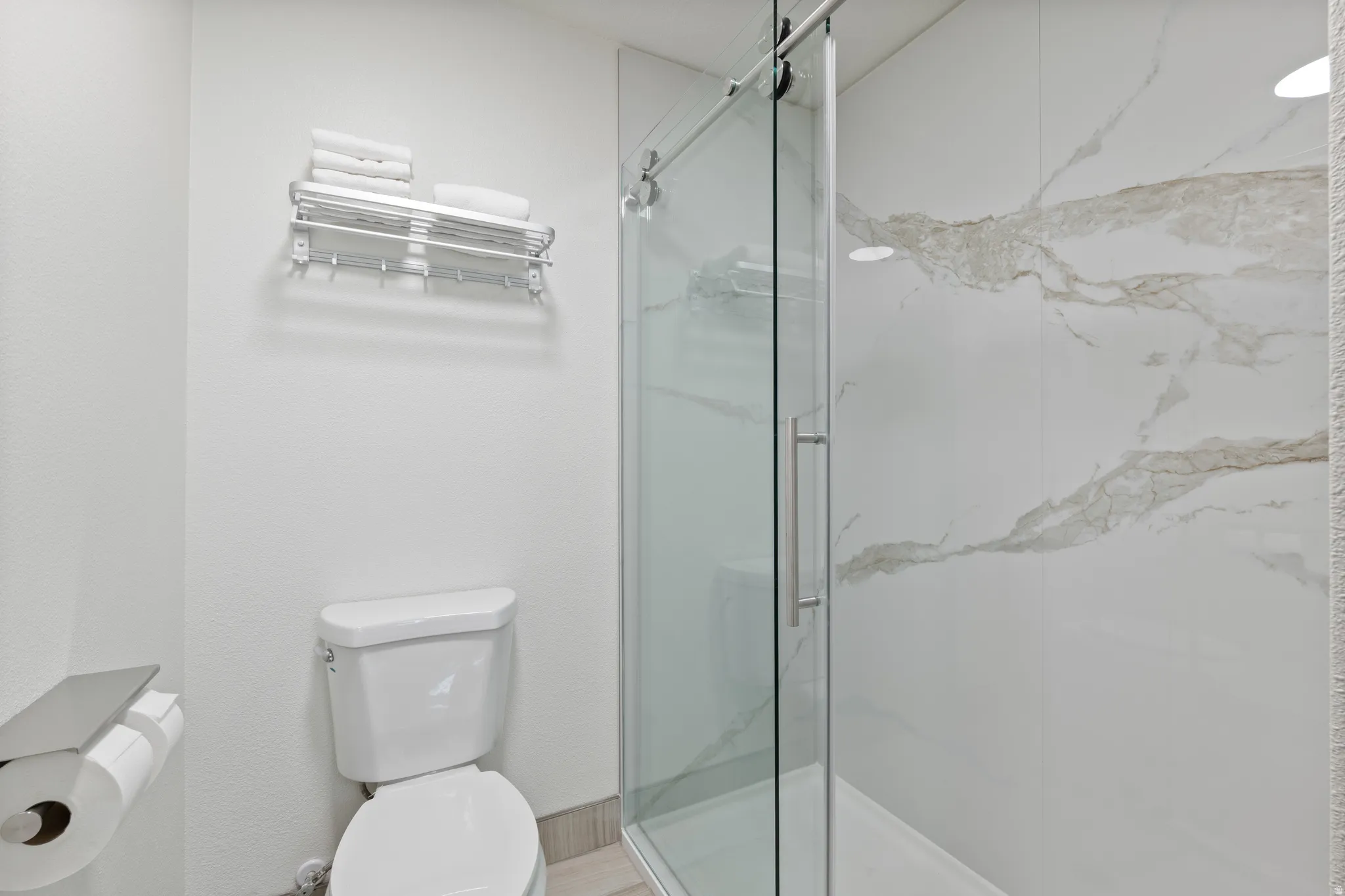 Glass-enclosed shower with a sliding door and white veined wall panels