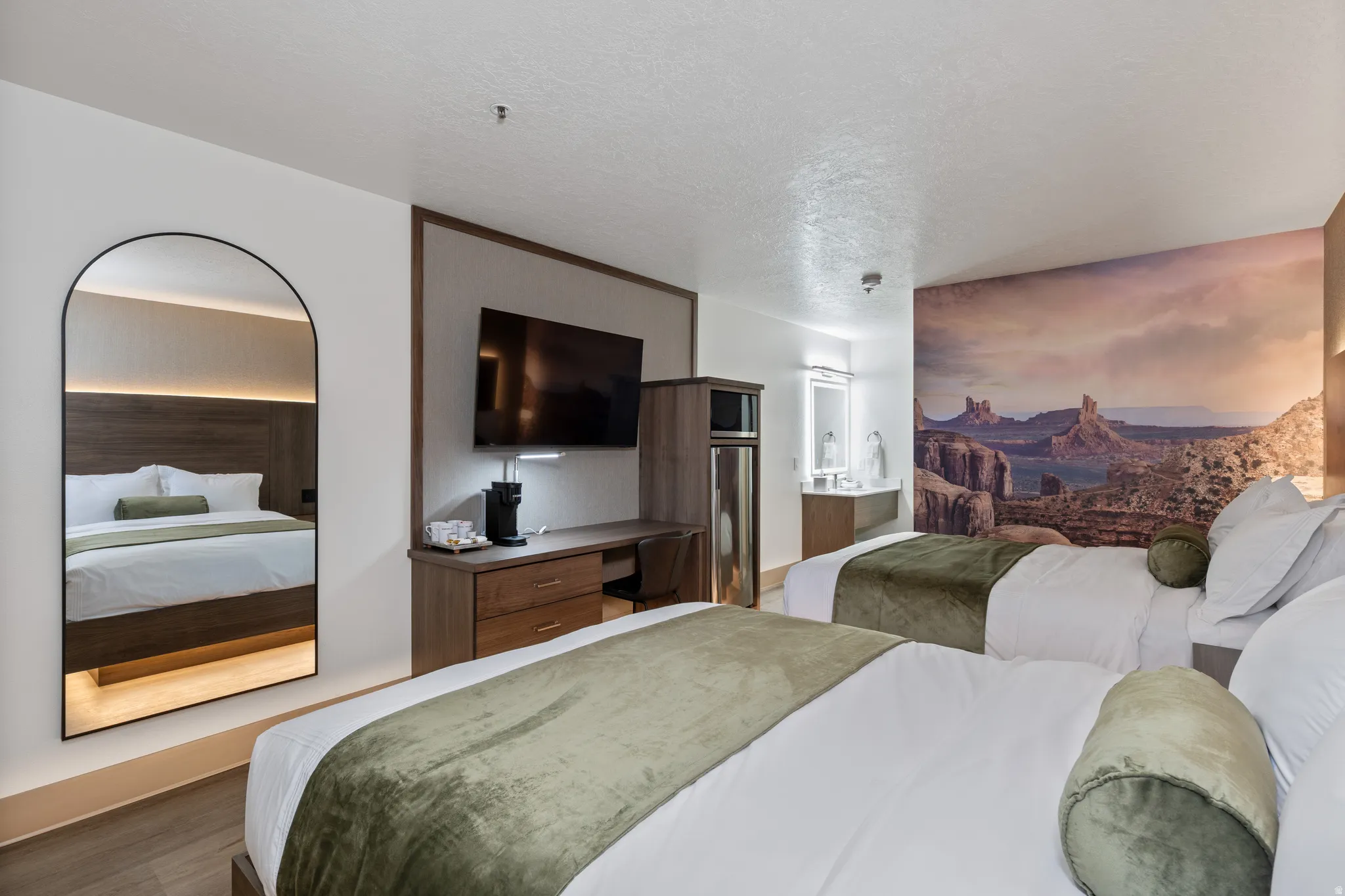 Bedroom featuring two beds with wood-finish headboards, a wall-mounted television, and a built-in wood-finish desk with drawers