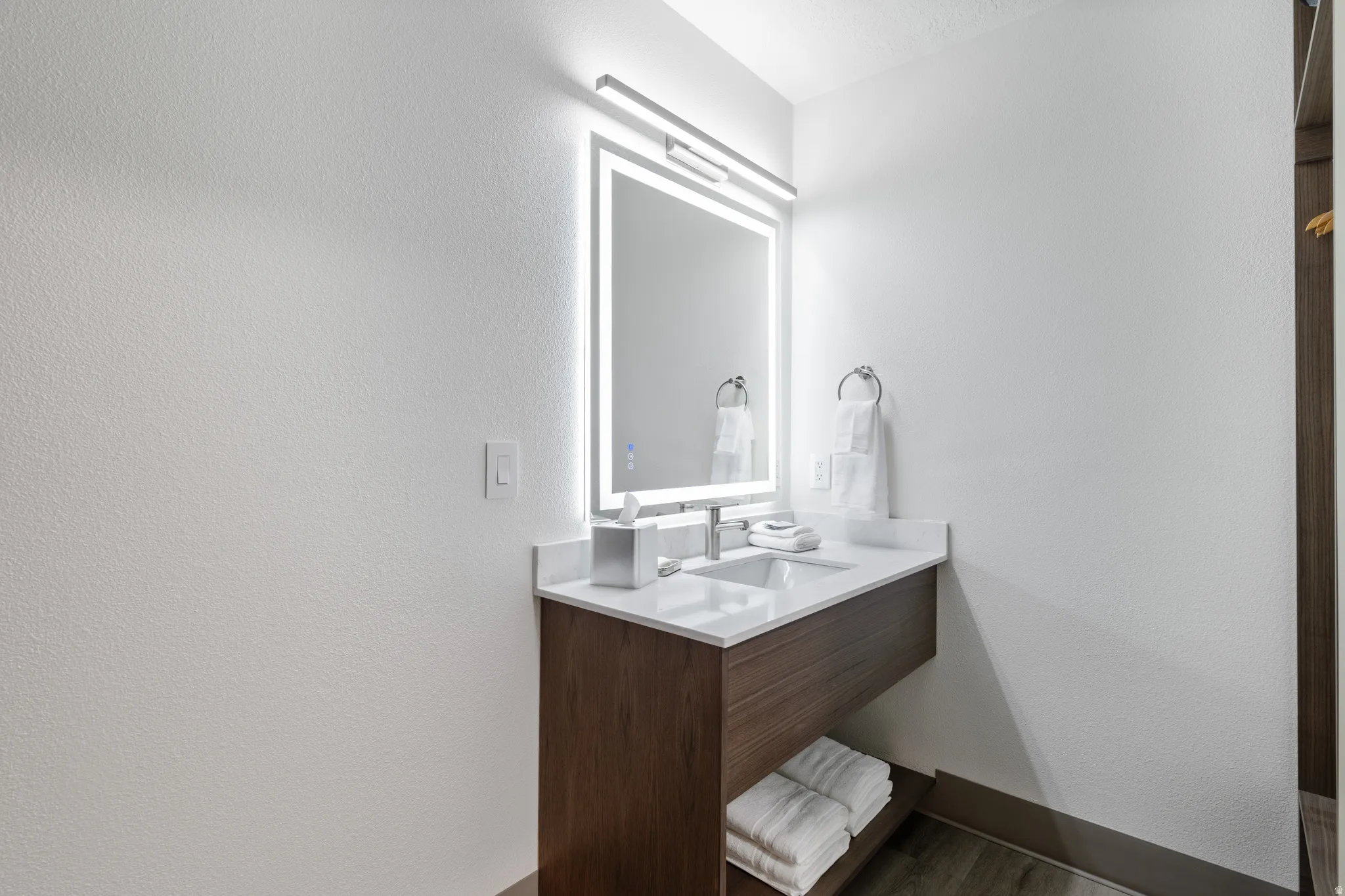 Vanity area featuring an illuminated mirror and a wood-finish floating vanity with an integrated sink