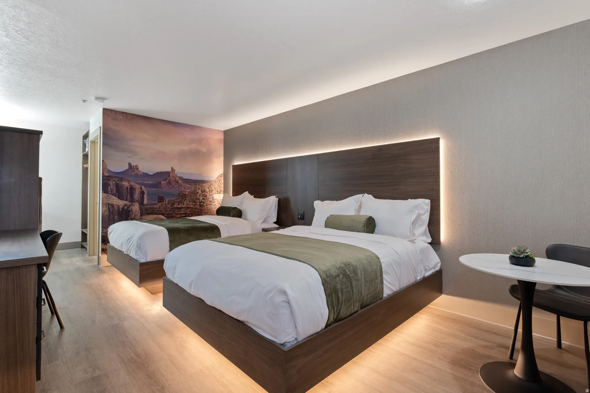 Bedroom featuring two platform beds, wood-finish flooring, a built-in wood-paneled headboard with integrated backlighting, a custom wall mural, and a dedicated desk area