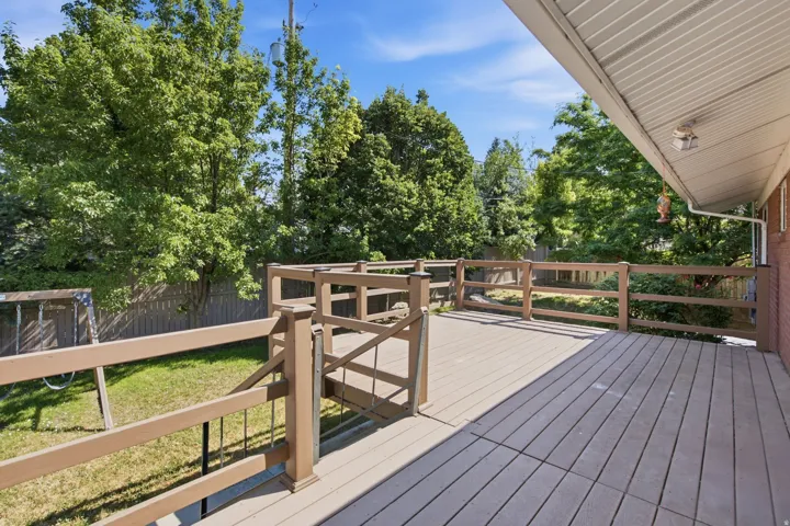 Spacious outdoor deck featuring composite decking, a wood railing with metal balusters, and mature perimeter trees