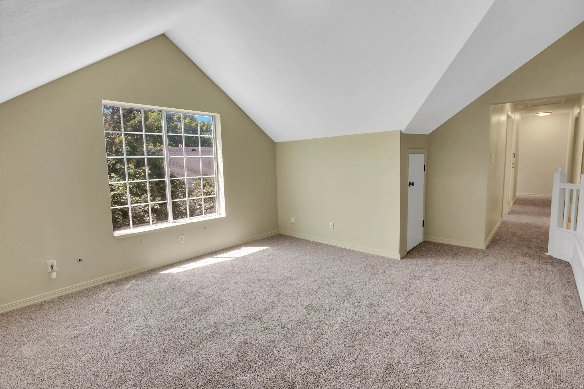Spacious room featuring vaulted ceilings, neutral-toned carpeting, and a large multi-pane window