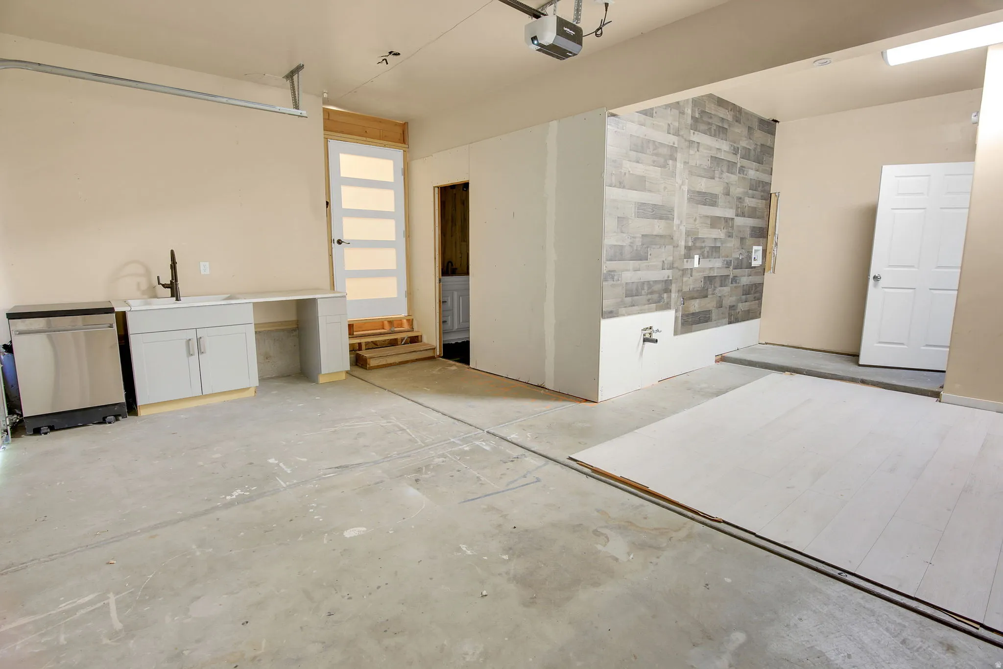 Concrete flooring garage with an integrated utility sink, base cabinetry, and a dishwasher unit