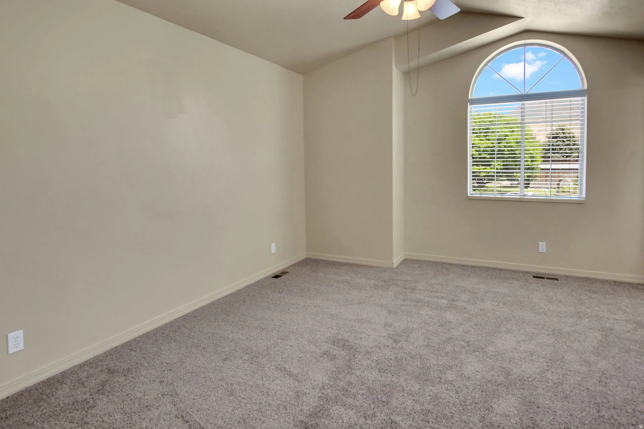 Arch-top window with horizontal blinds, sloped ceiling, ceiling fan with light fixture, and neutral-toned carpeting