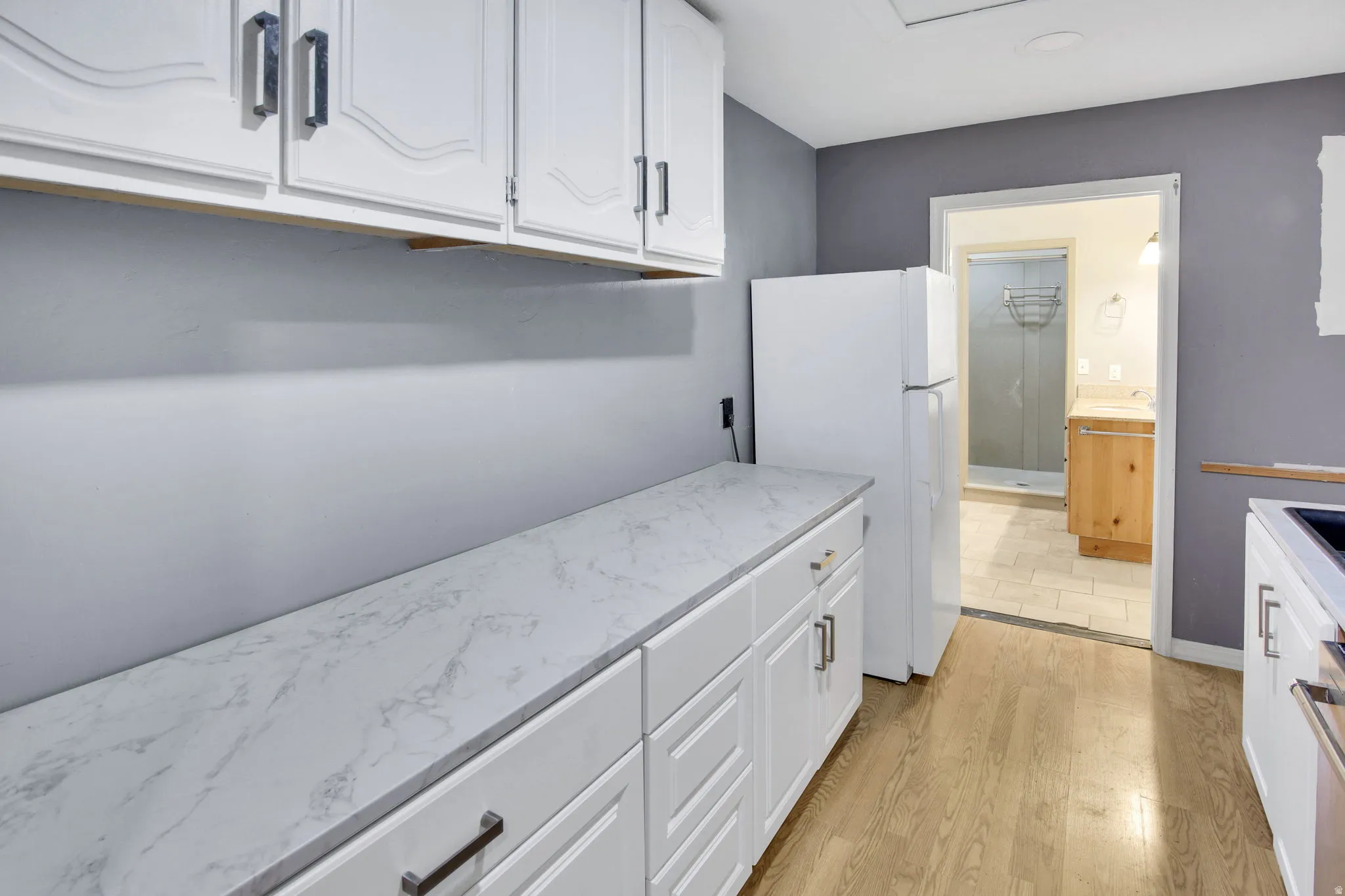 Kitchen featuring white cabinetry with dark pulls, wood-finish flooring, and light-toned countertops