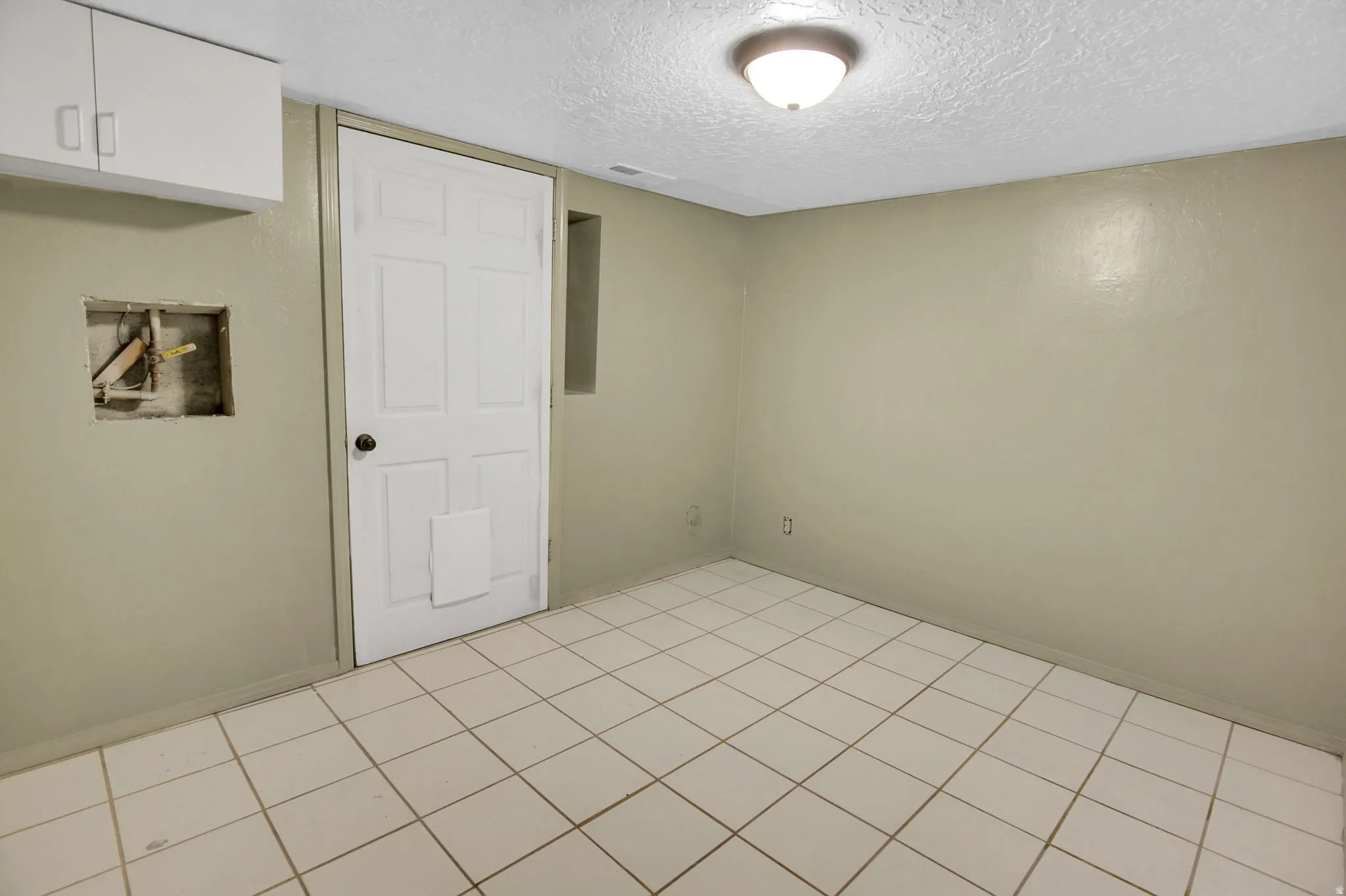 Room featuring light-colored walls, white square tile flooring, and a white six-panel door