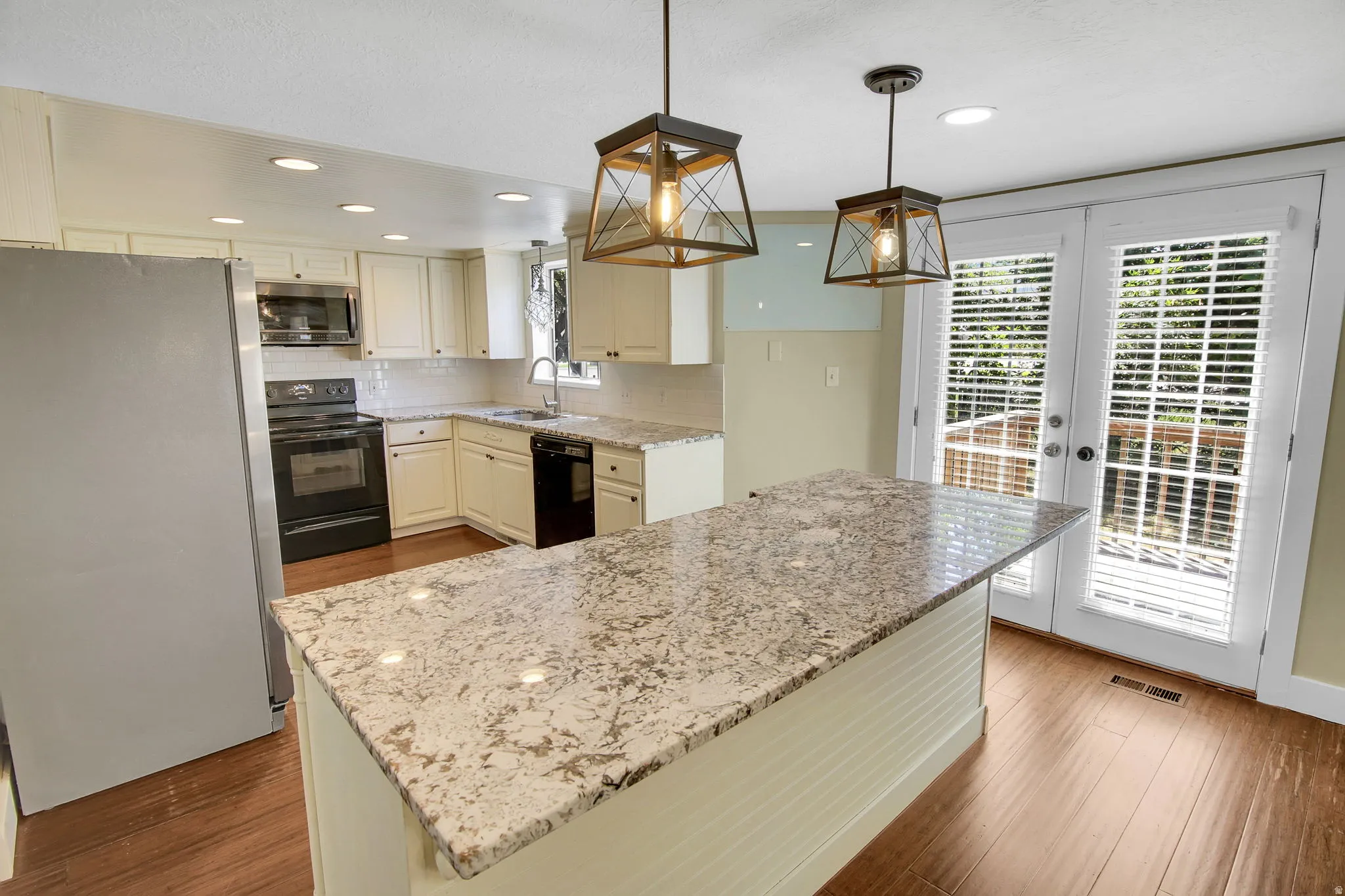Kitchen featuring a large central island with a light-toned countertop, white cabinetry, wood-finish flooring, recessed lighting, and double doors opening to an outdoor area
