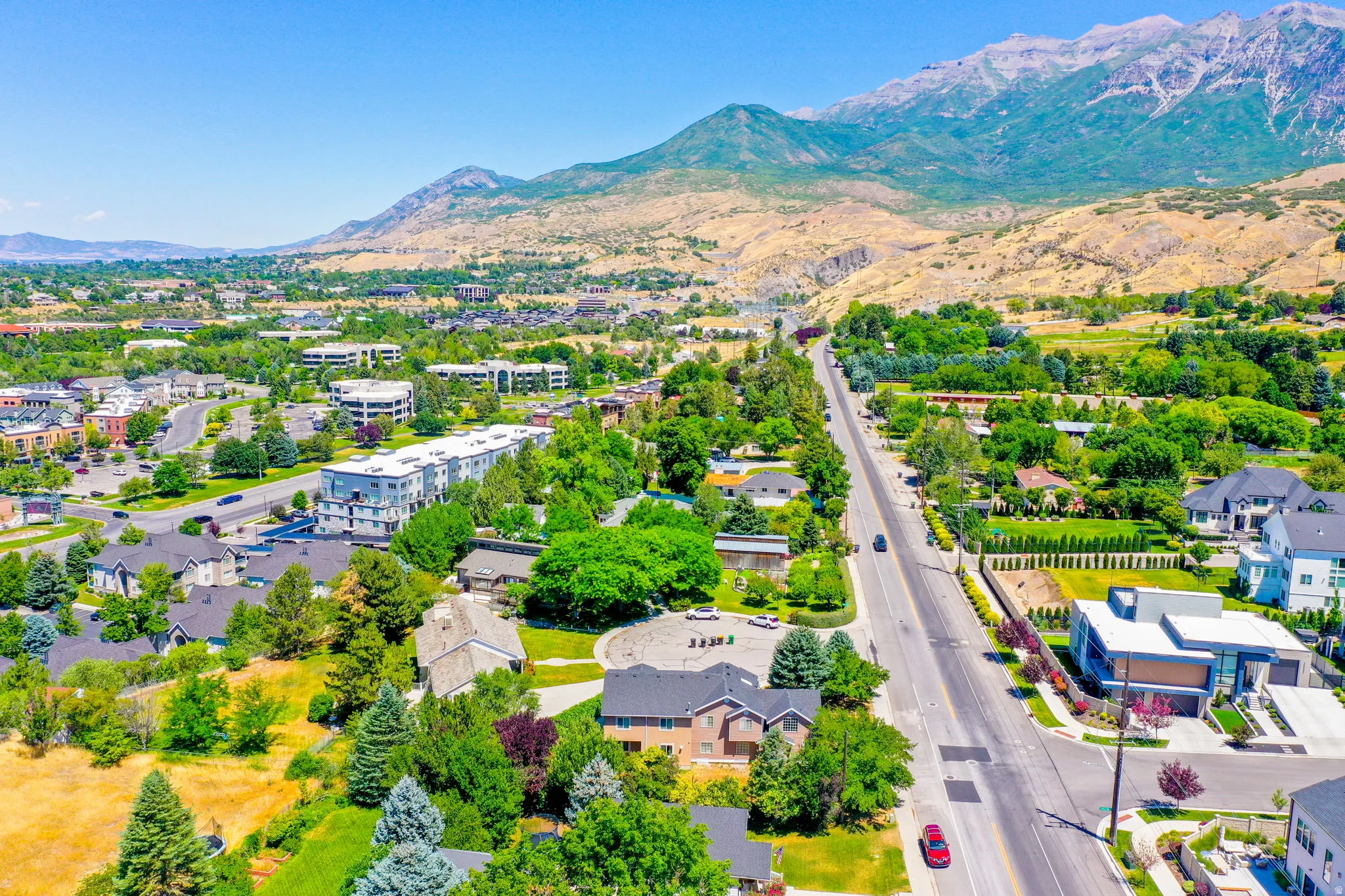 Expansive aerial landscape featuring a prominent mountain backdrop, lush green trees, and a clear blue sky