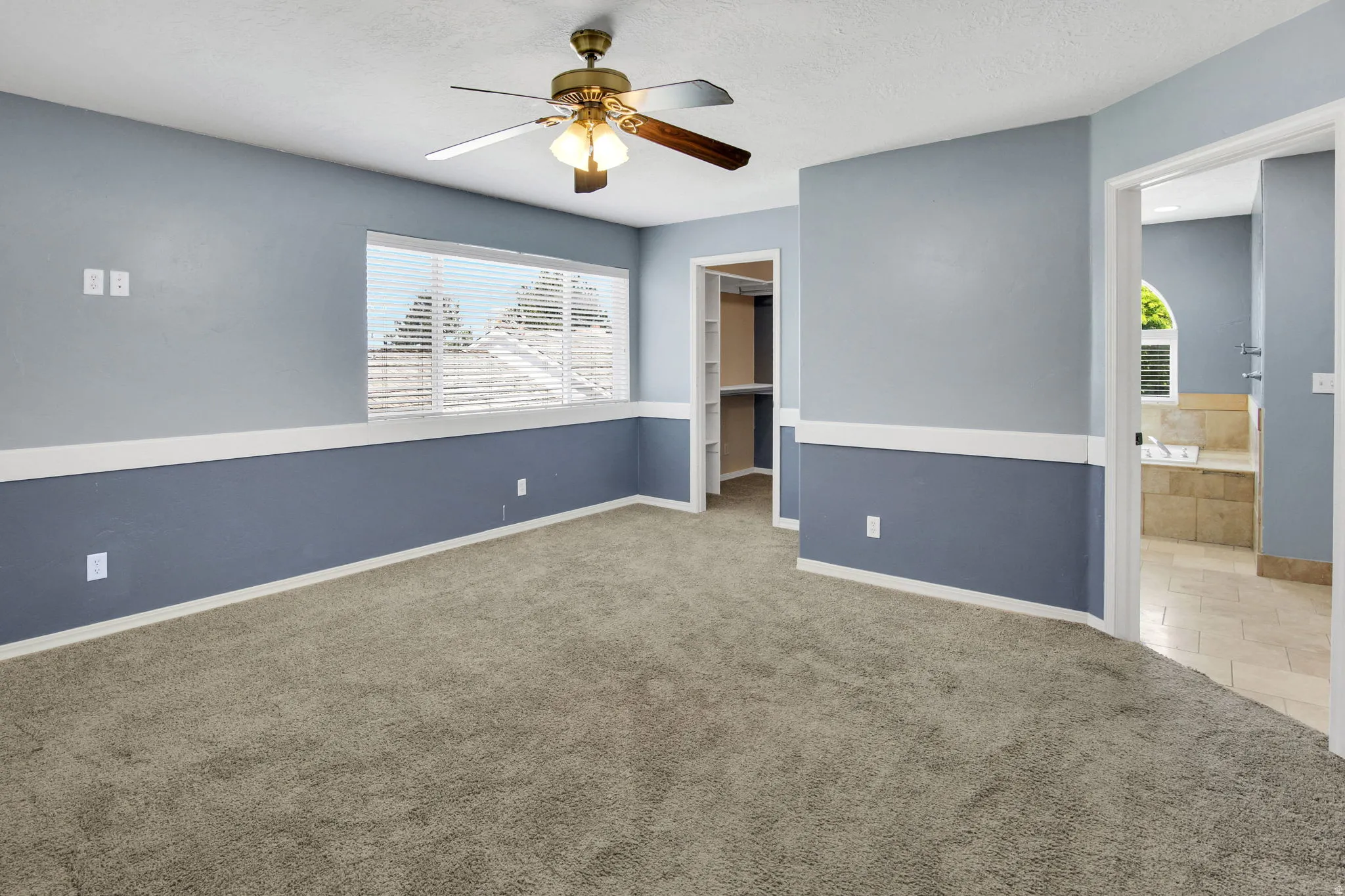 Carpeted interior space featuring a ceiling fan with light fixture, window with horizontal blinds, and a two-tone wall treatment