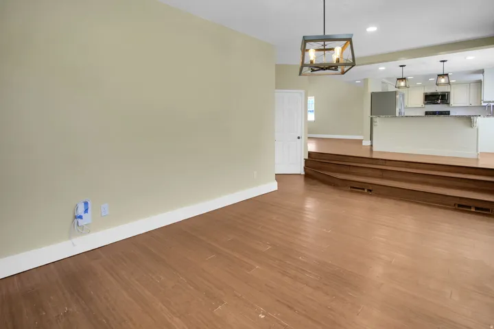 Spacious living area featuring wood-finish flooring, a contemporary chandelier, and a multi-level transition to a bright kitchen