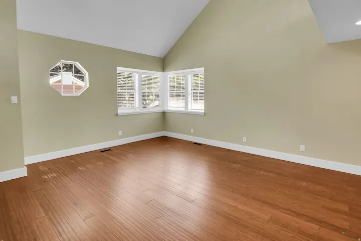 Spacious room featuring vaulted ceilings, wood-finish flooring, white baseboards, and a corner window arrangement with horizontal blinds