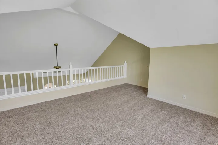 Carpeted loft area featuring a white railing, vaulted ceiling, and neutral-toned wall paint