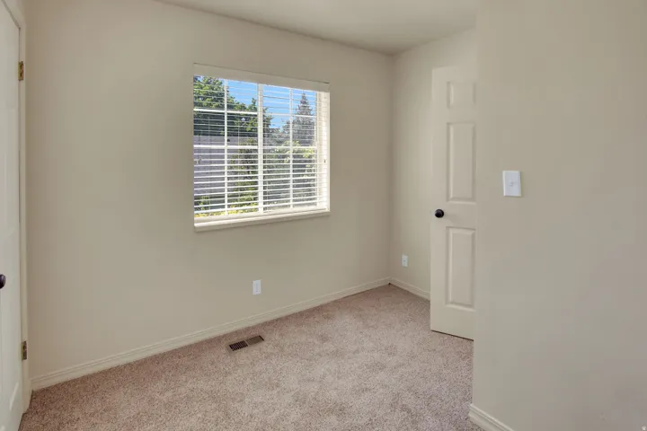 Neutral-toned room with plush carpeting, a window featuring horizontal blinds, and a paneled door with a round black doorknob