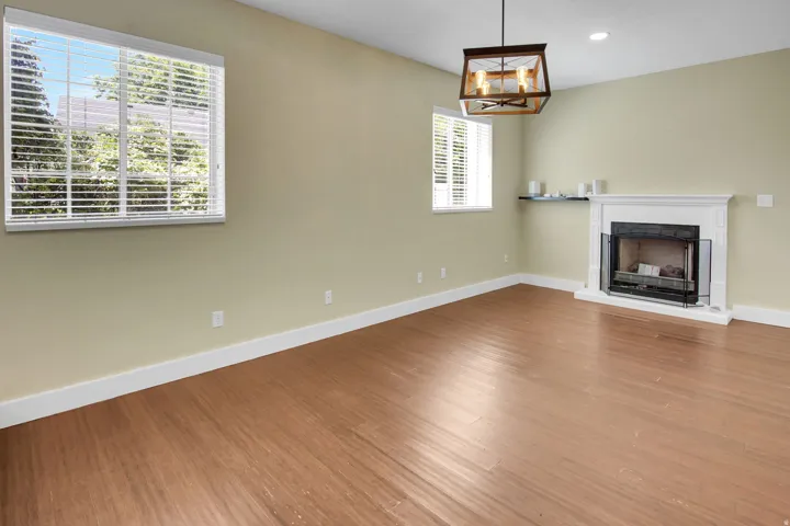 Spacious room featuring wood-finish flooring, a white mantel fireplace with a black screen, and a modern rectangular chandelier
