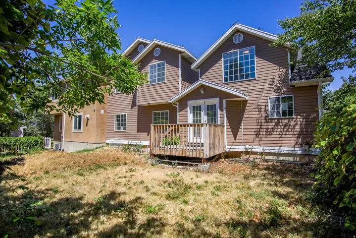 Rear exterior featuring a wood deck with railing, double French doors, large upper-level windows, and a multi-level design