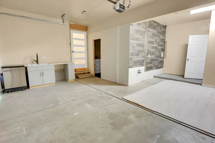 Concrete flooring garage with an integrated utility sink, base cabinetry, and a dishwasher unit