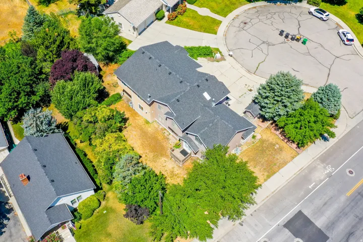Aerial perspective highlighting a residential property with a dark shingle roof and surrounding mature trees