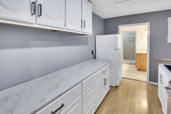 Kitchen featuring white cabinetry with dark pulls, wood-finish flooring, and light-toned countertops