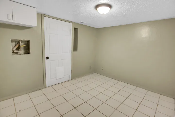 Room featuring light-colored walls, white square tile flooring, and a white six-panel door