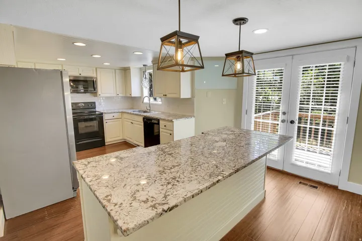 Kitchen featuring a large central island with a light-toned countertop, white cabinetry, wood-finish flooring, recessed lighting, and double doors opening to an outdoor area