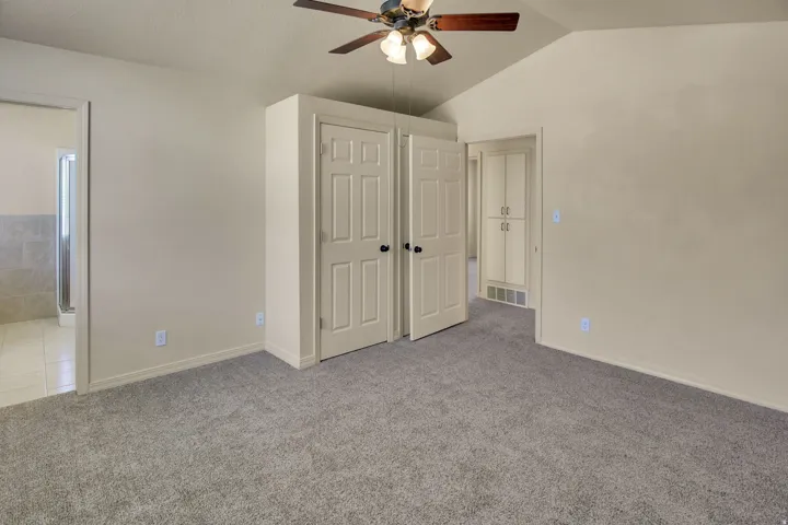 Carpeted room featuring a vaulted ceiling and a ceiling fan with integrated lighting
