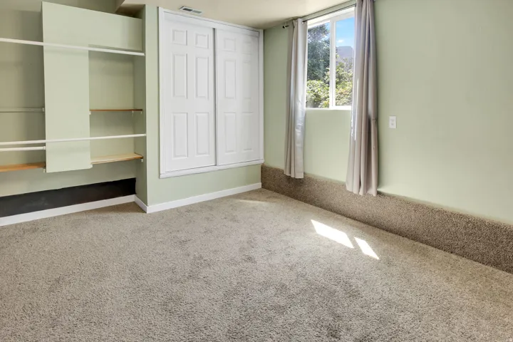 Carpeted room featuring a large window, built-in shelving, and a closet with sliding doors