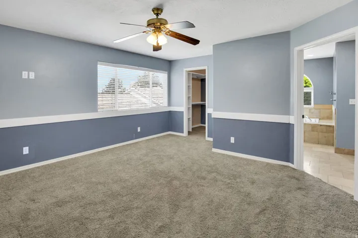 Carpeted interior space featuring a ceiling fan with light fixture, window with horizontal blinds, and a two-tone wall treatment